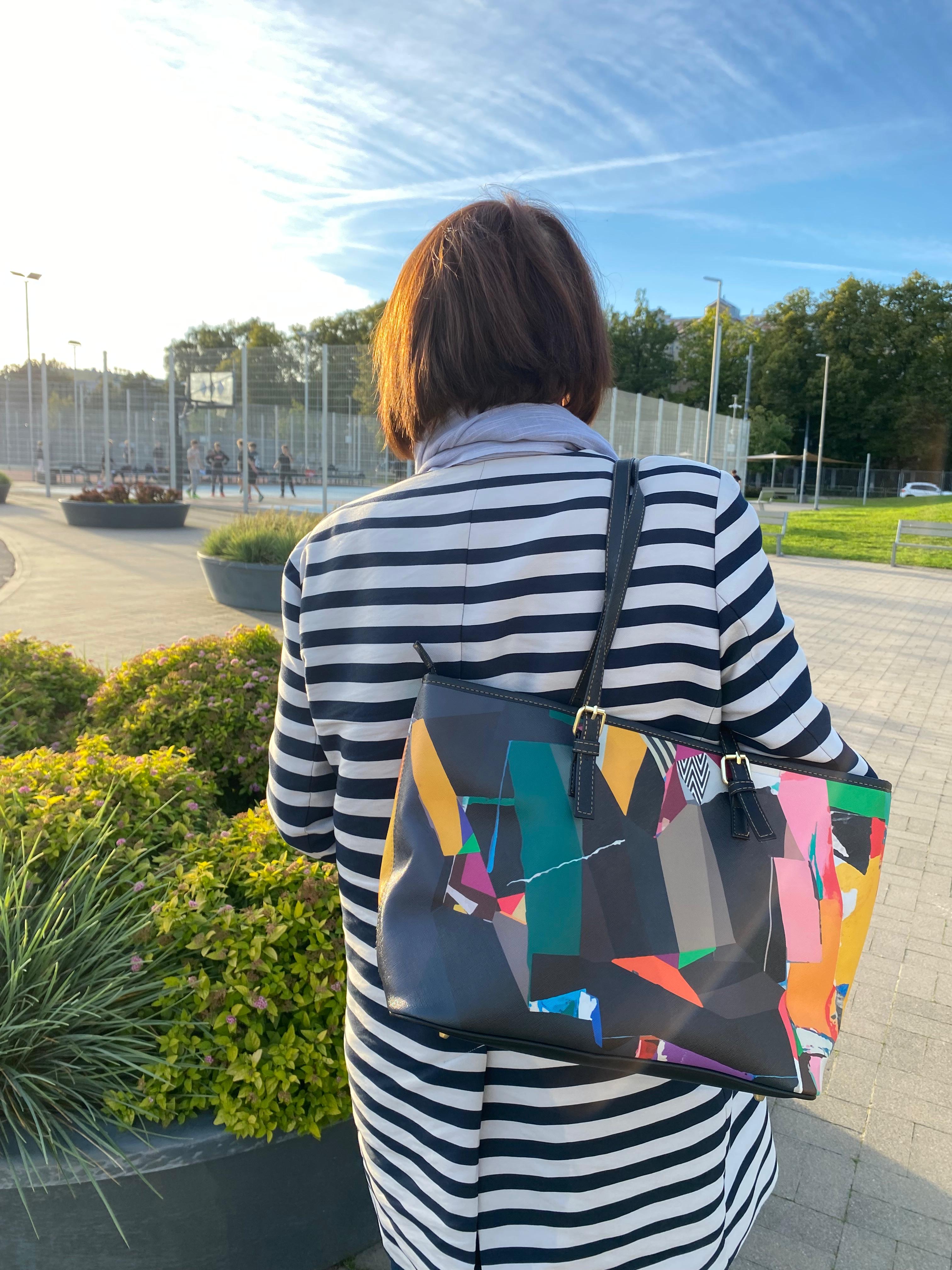 Model wearing a striped outfit paired with a colorful unique design handbag, artistic fashion accessories, modern wearable art style, creative statement look photographed outdoors in natural light