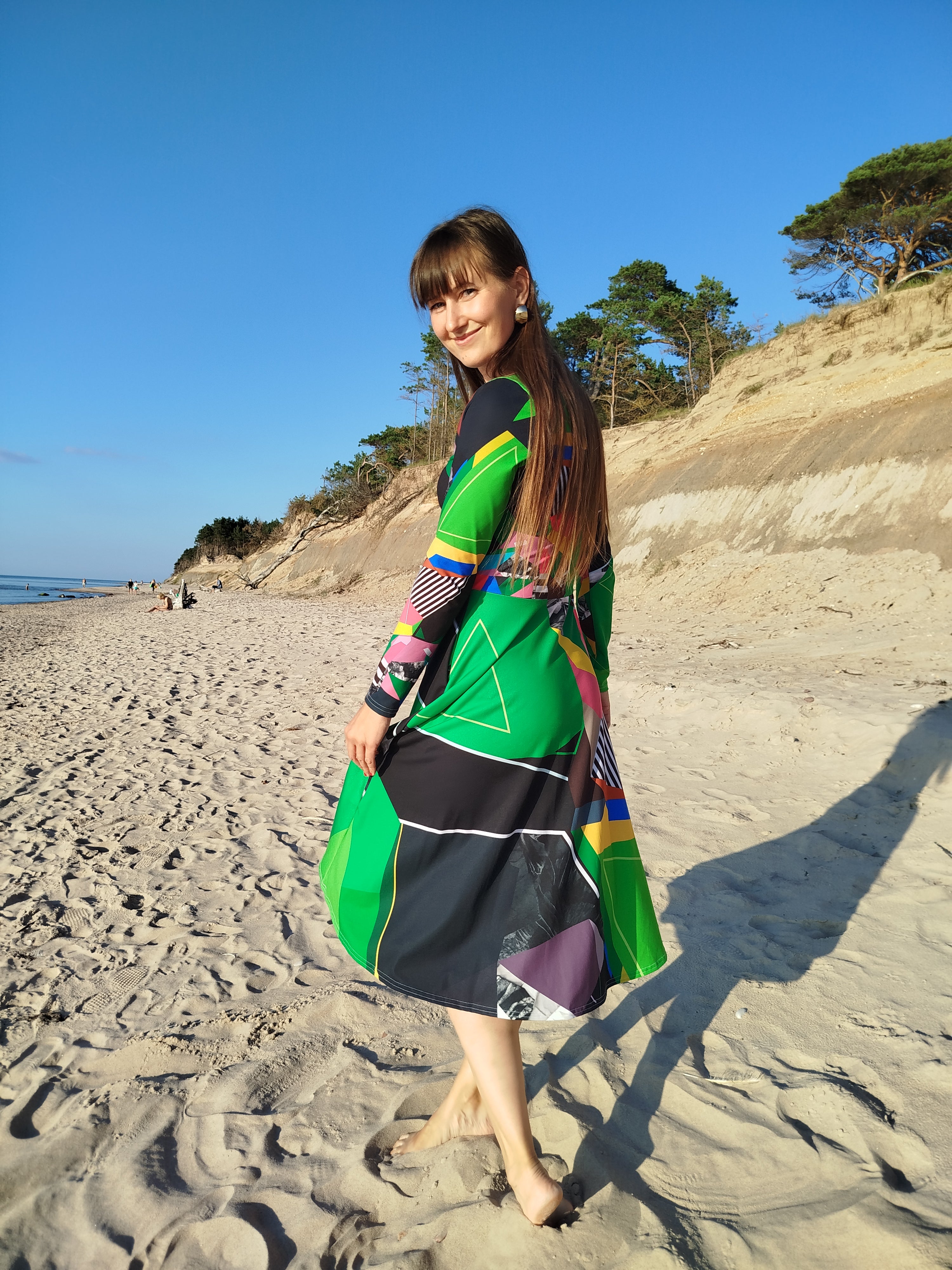 Woman walking in a green abstract midi dress with long sleeves, flowing artistic patterned skirt, modern feminine statement dress