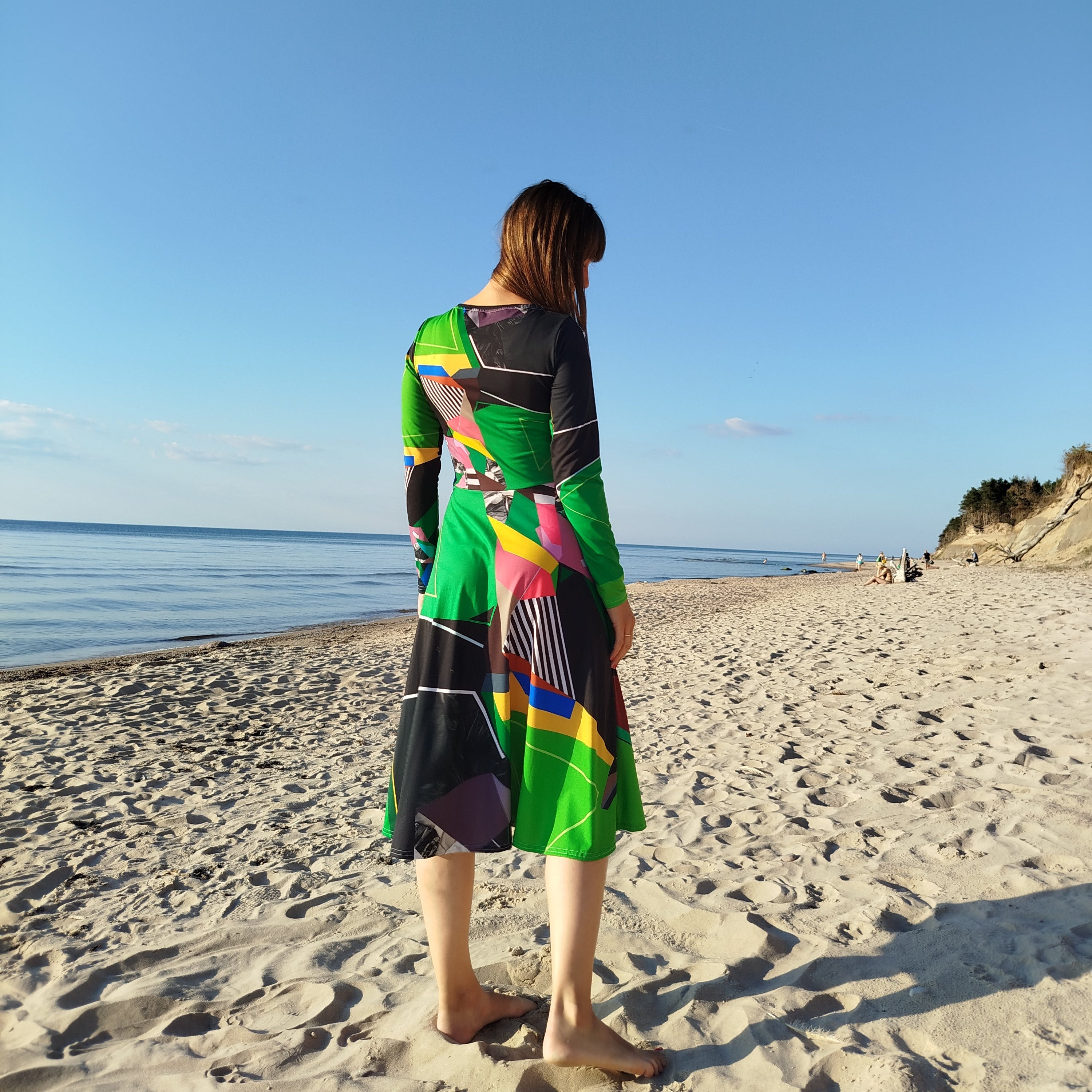 Green abstract midi dress with long sleeves styled outdoors, artistic patterned midi dress for women photographed on a sandy beach under a bright blue sky