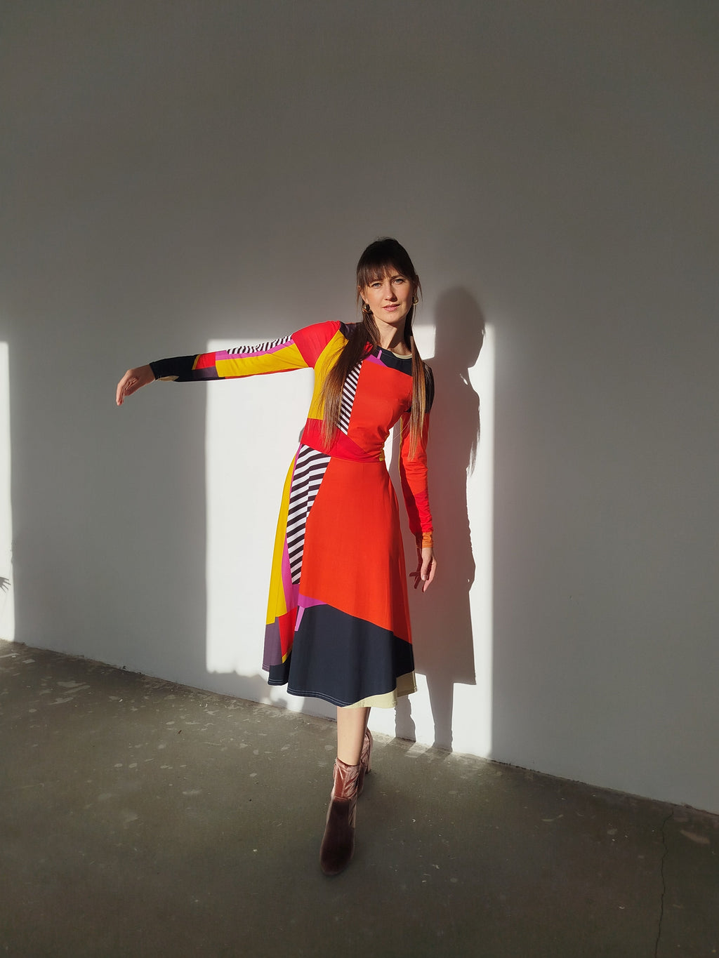 Woman moving gracefully in a vibrant abstract-print midi dress, red and yellow panels glowing as the skirt lifts and flows during her dance.