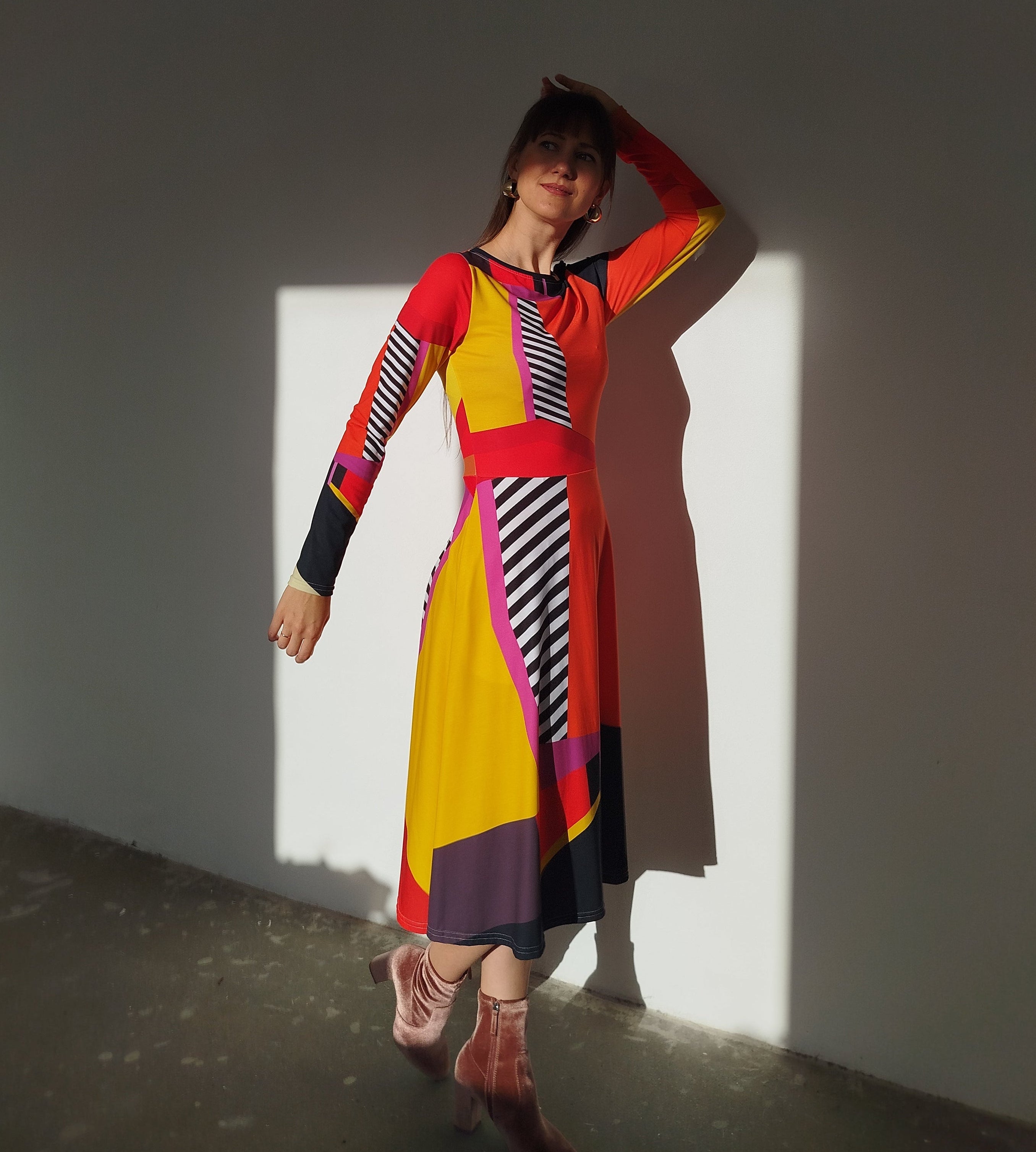 Eye-catching geometric midi dress with bright red and golden yellow panels, black-and-white stripes, and contrast trim, long sleeves and tailored waist creating a striking contemporary silhouette. With long sleeves and pockets.