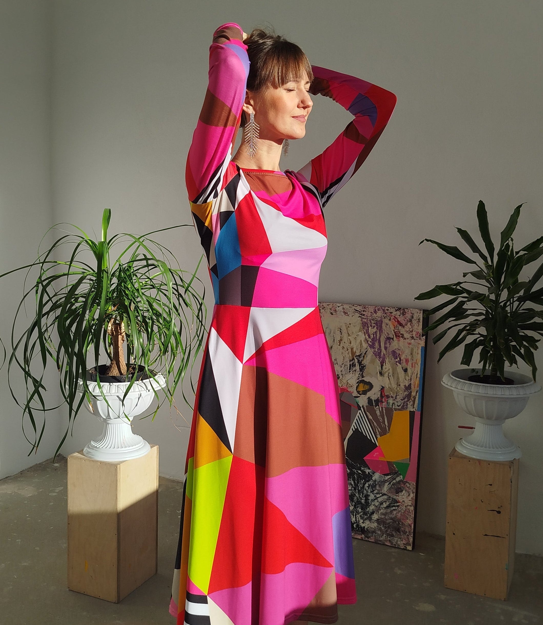 Woman wearing a pink colorful geometric dress standing in a room with plants and abstract art.