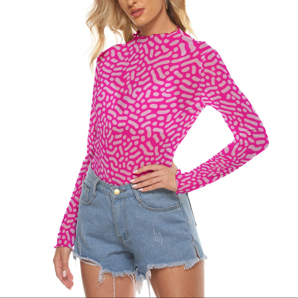 A woman modeling a bright pink long-sleeve mock-neck top with a light pink abstract wavy pattern, paired with light-wash denim shorts, against a solid white background.