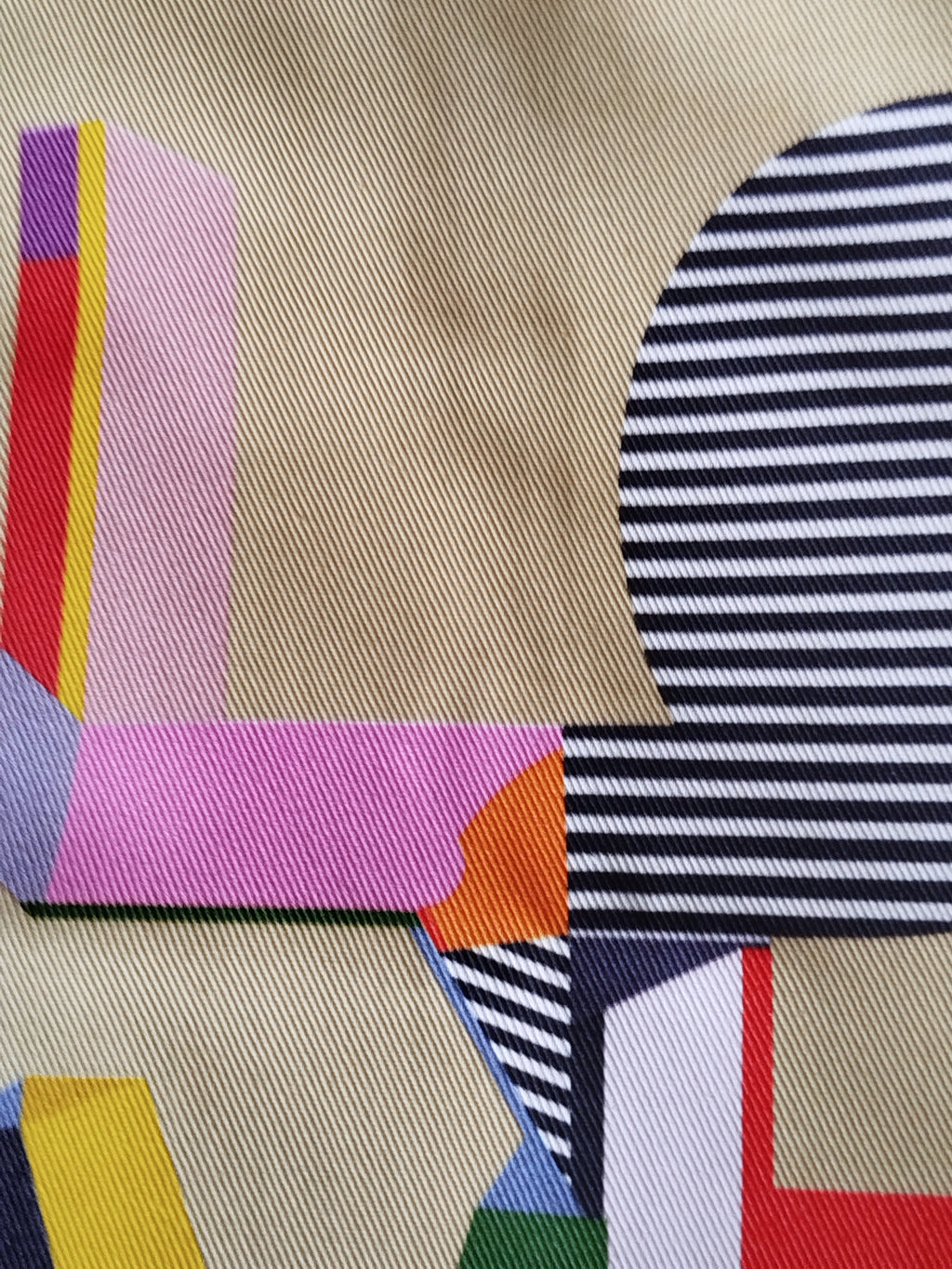 A close-up of a patterned fabric featuring a geometric design with navy blue and white stripes, a beige base, pink, yellow, orange, red, and purple blocks.