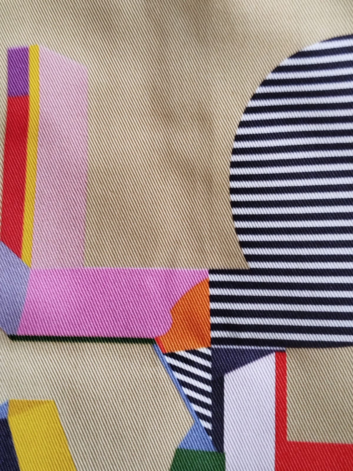 A close-up of a patterned fabric featuring a geometric design with navy blue and white stripes, a beige base, pink, yellow, orange, red, and purple blocks.