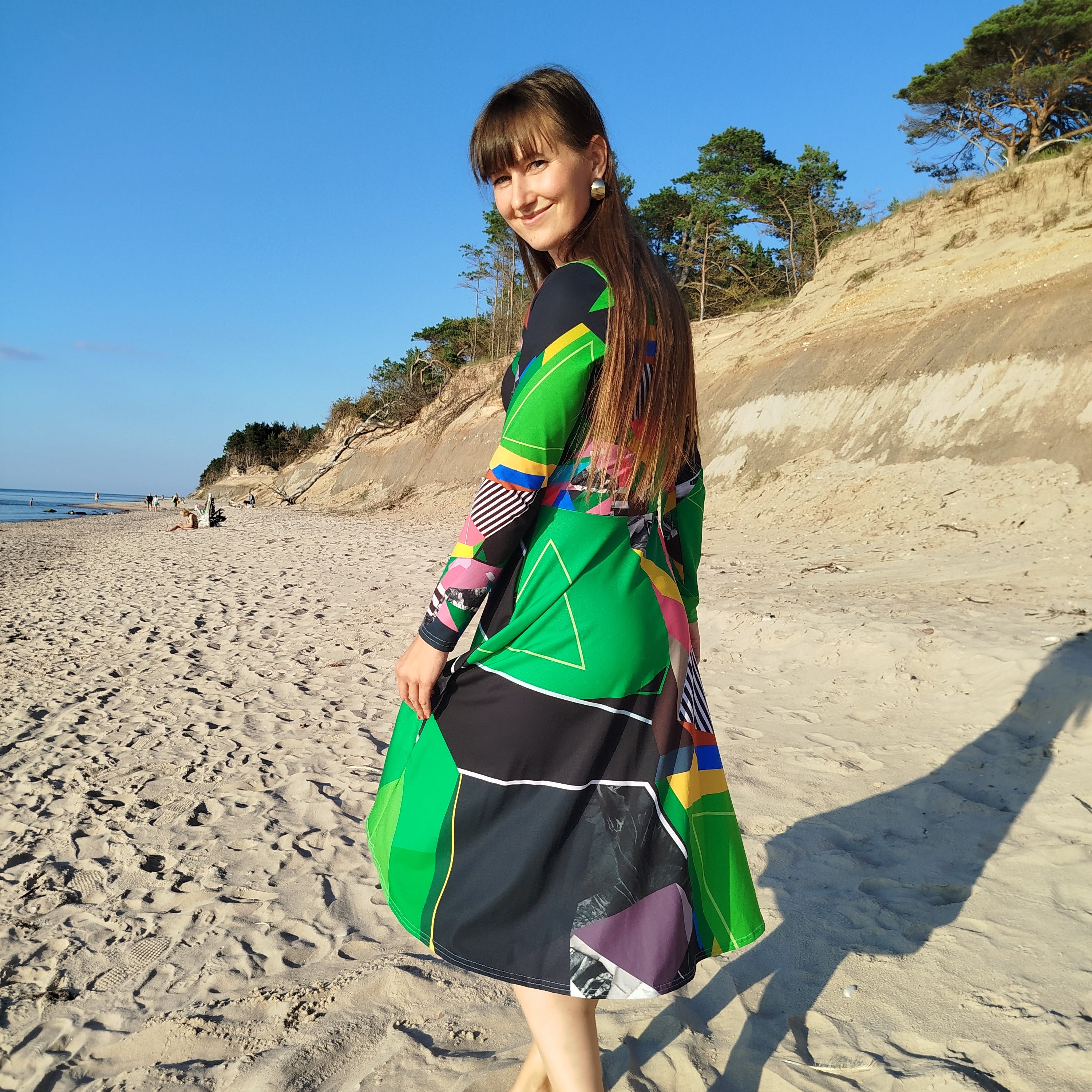 Woman walking in a green abstract midi dress with long sleeves, flowing artistic patterned skirt, modern feminine statement dress
